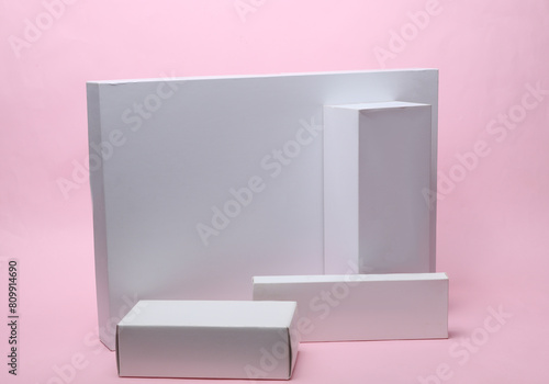 Different shapes of white cardboard boxes for presentation products on pink background. Mockup for design.