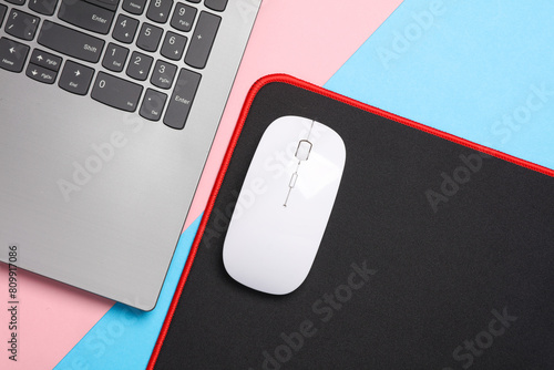 Laptop and PC mouse with PC mouse pad on pink blue background. Top view