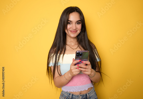 Portrait of a smiling casual woman holding smartphone over yellow background