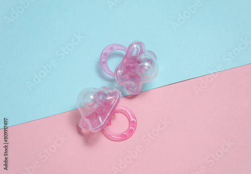 Two baby pacifiers on a blue-pink background. Flat lay