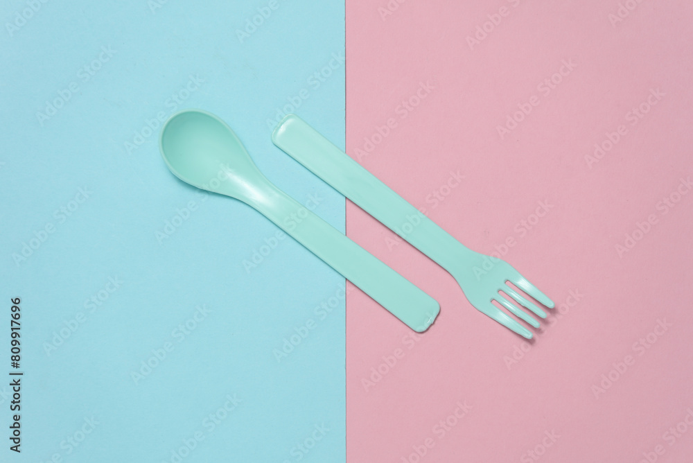 Plastic fork and spoon for baby on a blue pink background. Top view Plastic fork and spoon for baby on a blue pink background. Top view