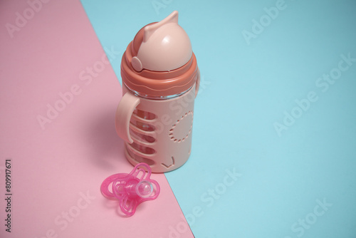 Drinking bowl and Baby pacifier for baby on a blue-pink background. Top view