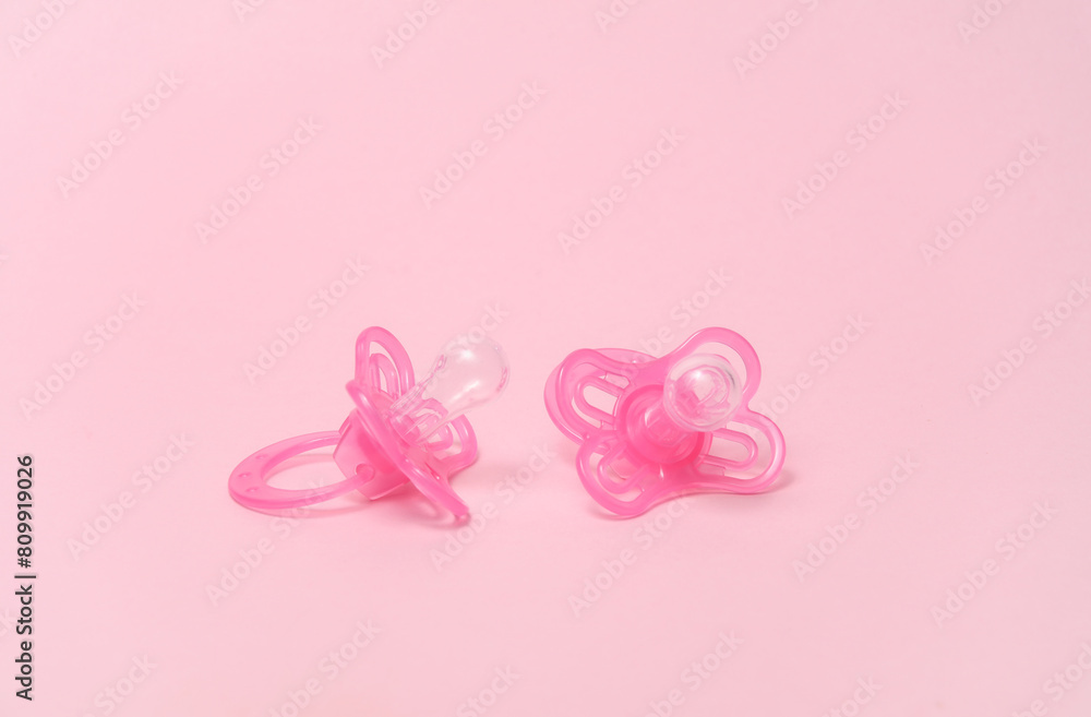 Two baby pacifiers on a pink background.
