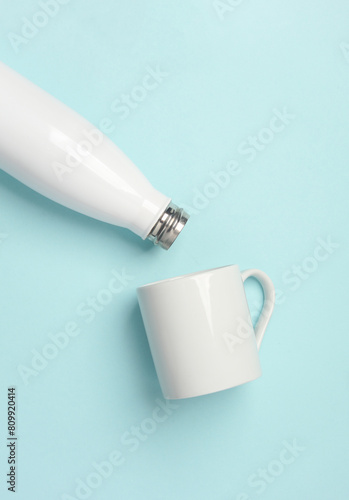 Mockup of white empty ceramic cup and thermos bottle on blue blue background photo