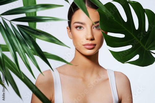 Beauty woman portrait with tropical leaves, on bright background 