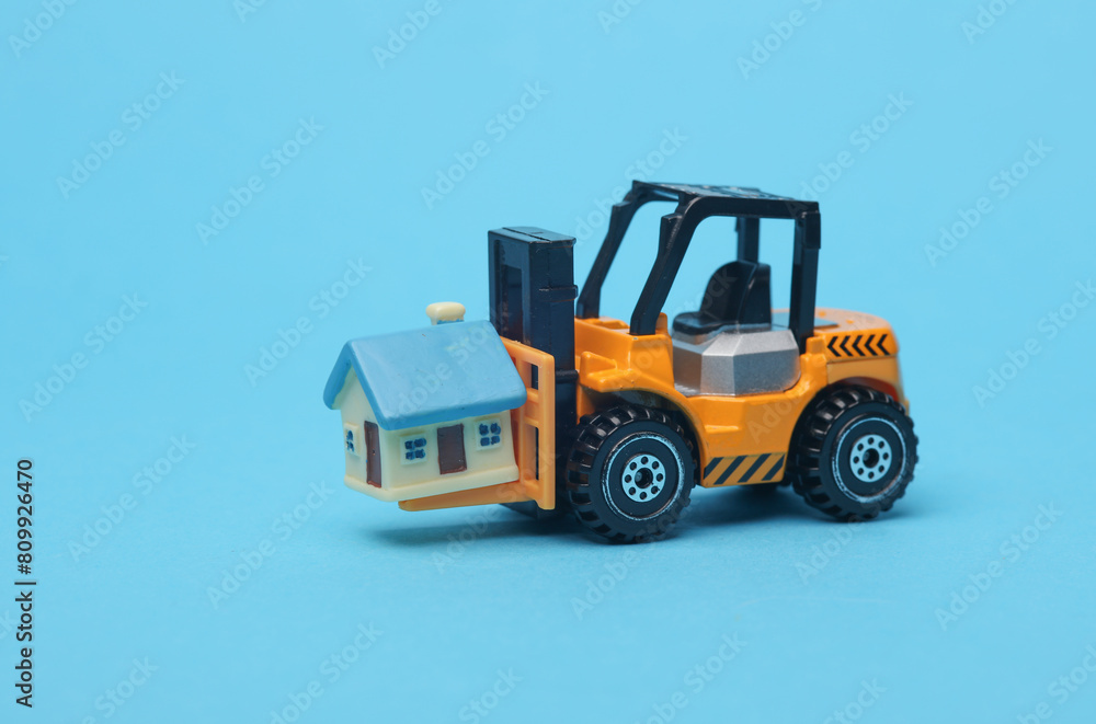 Forklift miniature with house model on blue background Forklift miniature with house model on blue background
