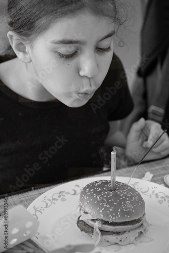 High resolution close up portrait image of a young girl blowing her birthday candle on a cheese burger- Israel
