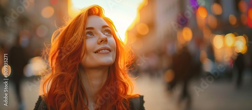 Happy beautiful charming young woman with red hair in the City streets sunset looking up