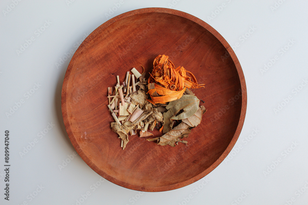 Wedang Uwuh, or Javanese herbal drink, isolated on white background. Ingredients before brewed of Indian redwood, dried ginger, lemongrass and cardamom. On wooden plate Wedang Uwuh, or Javanese herbal drink, isolated on white background. Ingredients before brewed of Indian redwood, dried ginger, lemongrass and cardamom. On wooden plate