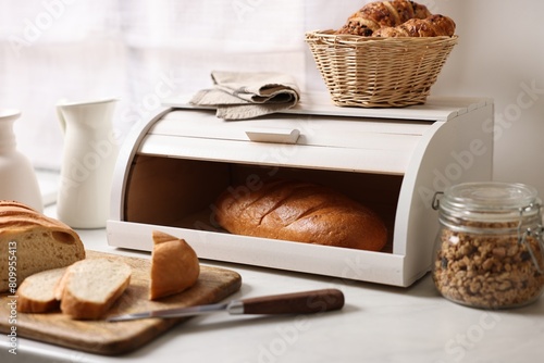 Wooden bread basket with freshly baked loaves on white marble table in kitchen photo