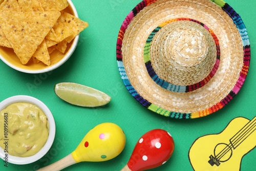 Mexican sombrero hat  nachos chips  guacamole  maracas  lime and paper guitar on green background  flat lay