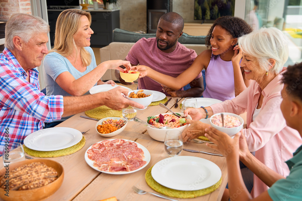 Three Generation Family Indoors Around Table At Home Serving And Eating Meal Together Three Generation Family Indoors Around Table At Home Serving And Eating Meal Together