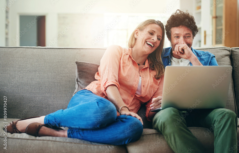Mature, couple and laughing with laptop on sofa for comedy movie, funny series or streaming service in home. People, technology and comic video on couch with relax, bonding or entertainment in lounge