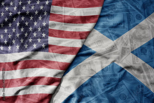 big waving colorful flag of united states of america and national flag of scotland on the dollar money background. finance concept. photo
