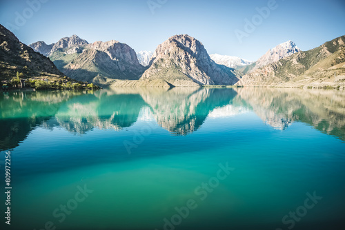 Panoramic view of blue Iskanderkul lake and rocky mountains in Tajikistan, the mountain range is reflected in the water of the lake in the early morning photo