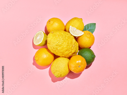 Fruits frais de la Méditerranée, agrumes disposés sur fond rose avec cédrat, citron vert, citron jaune, bergamote, demi citron coupé et quartier de citron, lumière solaire,  photo