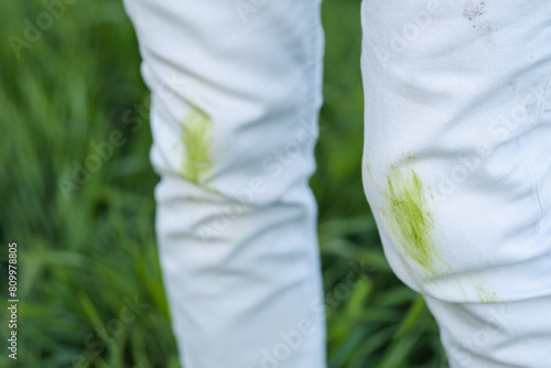 Close up dirty grass stains on white clothes. An unrecognizable person with green knees on a green background. Spoiled clothes. Ecological methods of stain removal. outdoors. 