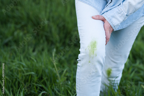Dirty grass stains on white clothes. An unrecognizable person with green knees on a green background. Spoiled clothes.
