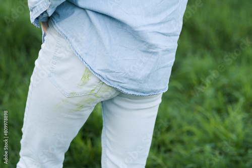 Close up dirty grass stains on white clothes. An unrecognizable person with dirty grass stains pants on a green background, back turned. Spoiled clothes. Daily life dirty stain.outdoors. 