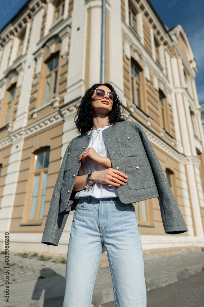 Fashionable beautiful stylish girl model in fashion summer clothes with a jacket, white T-shirt and jeans posing near a vintage building on the street Fashionable beautiful stylish girl model in fashion summer clothes with a jacket, white T-shirt and jeans posing near a vintage building on the street