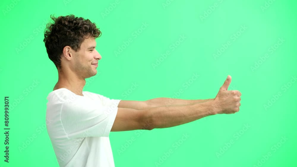 A man in a white T-shirt, on a green background, close-up, shows his thumbs up A man in a white T-shirt, on a green background, close-up, shows his thumbs up