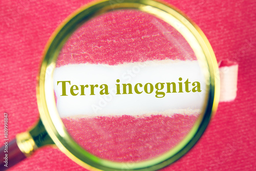 Terra incognita the phrase means unknown land through a magnifying glass under a piece of torn paper photo