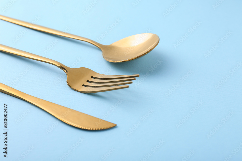Stylish golden cutlery set on light blue background, closeup. Space for text