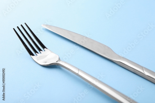 Stylish cutlery. Silver knife and fork on light blue background, closeup