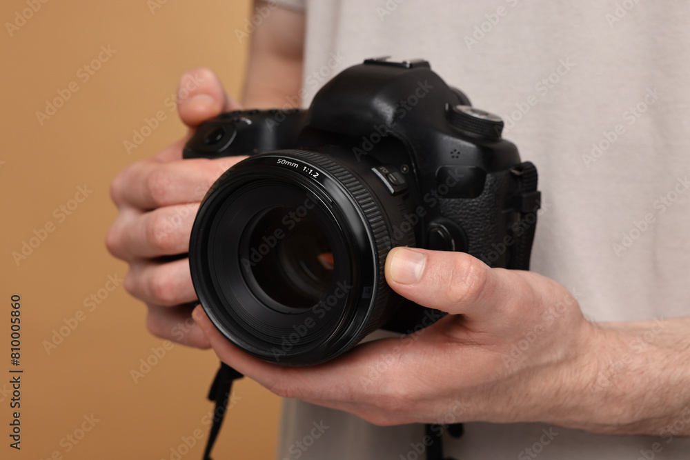 Photographer holding camera on beige background, closeup