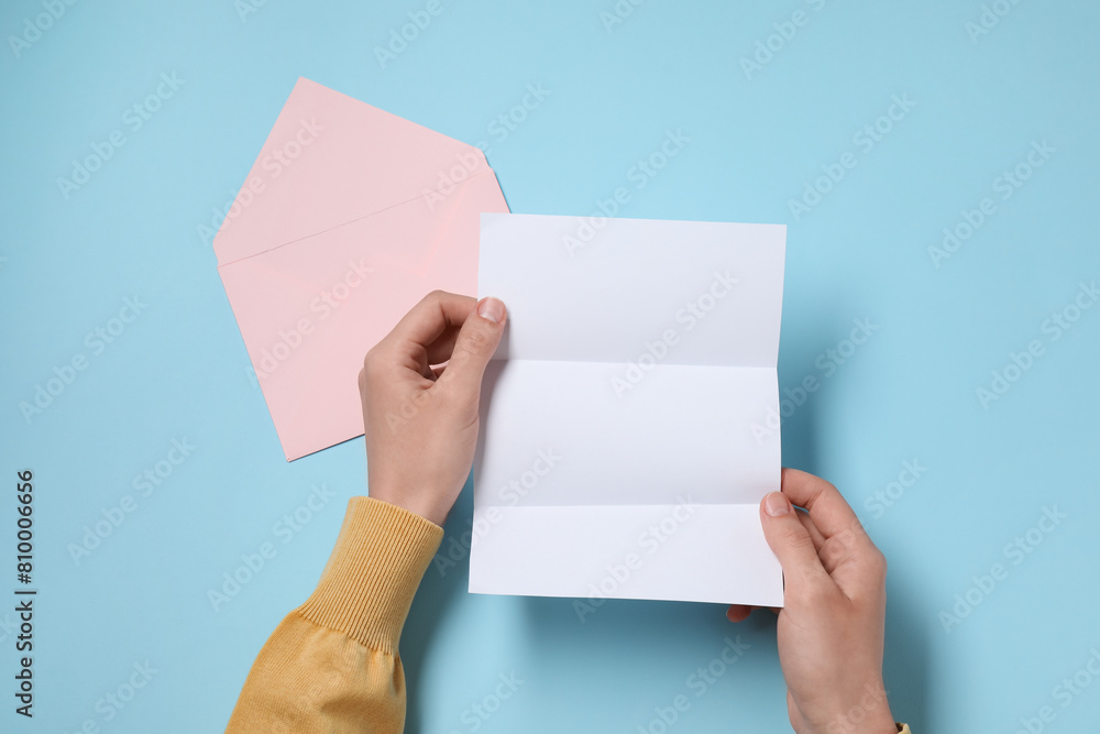 Woman with blank sheet of paper at light blue table, top view. Space for text Woman with blank sheet of paper at light blue table, top view. Space for text