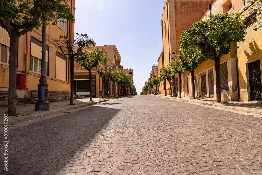 Fototapeta premium main pedestrian street of a typical Sicilian village in the early afternoon sun; no people; a small dog