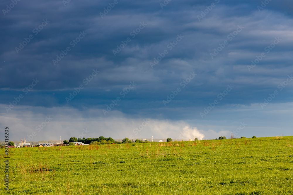 Sunny landscape against a dramatic sky, countryside in early spring, young green grass in a field Sunny landscape against a dramatic sky, countryside in early spring, young green grass in a field