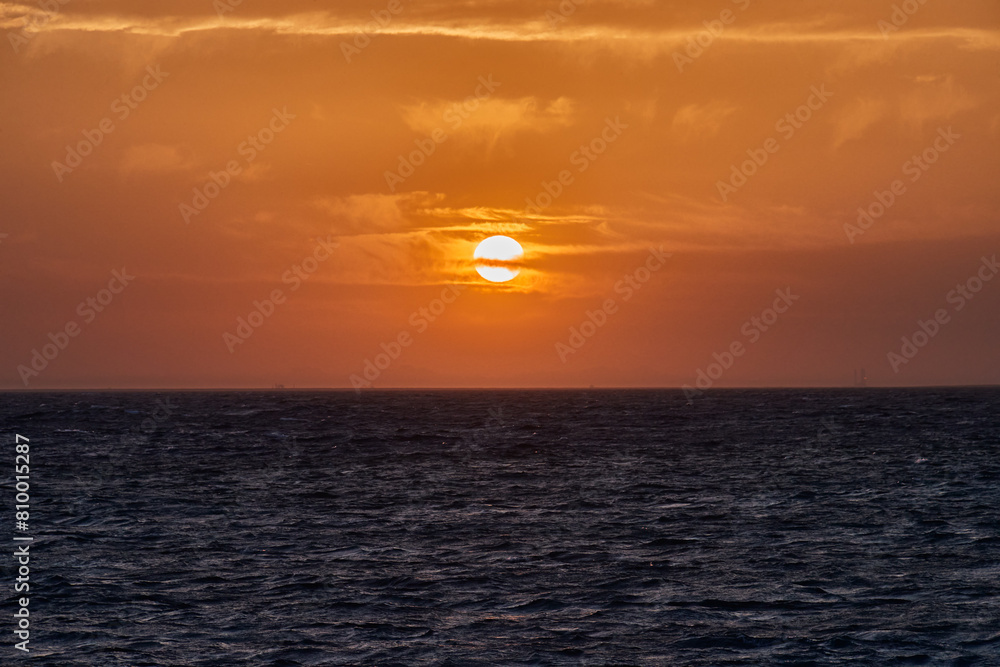 Cloudy orange sunset on dark ocean