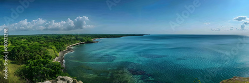 A long, winding coastline with lush green vegetation and a calm blue sea under a clear sky, captured in panoramic view