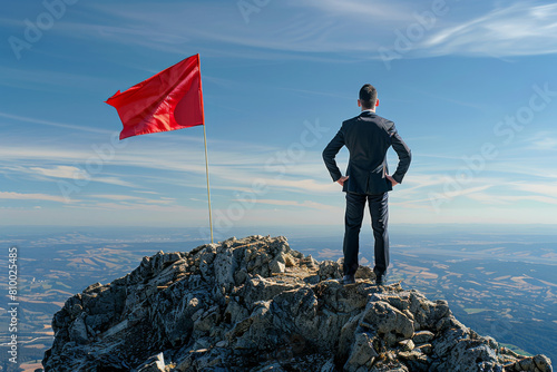 A businessman and a red flag on top of a mountain, leadership and success concept