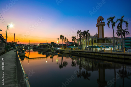 Al Eiatisom Mosque is located at Soi Anamai, Srinakarin Road, Bangkok, Thailand. The backdrop of the sunset is a two-tone blue sky with an orange and blue sky.