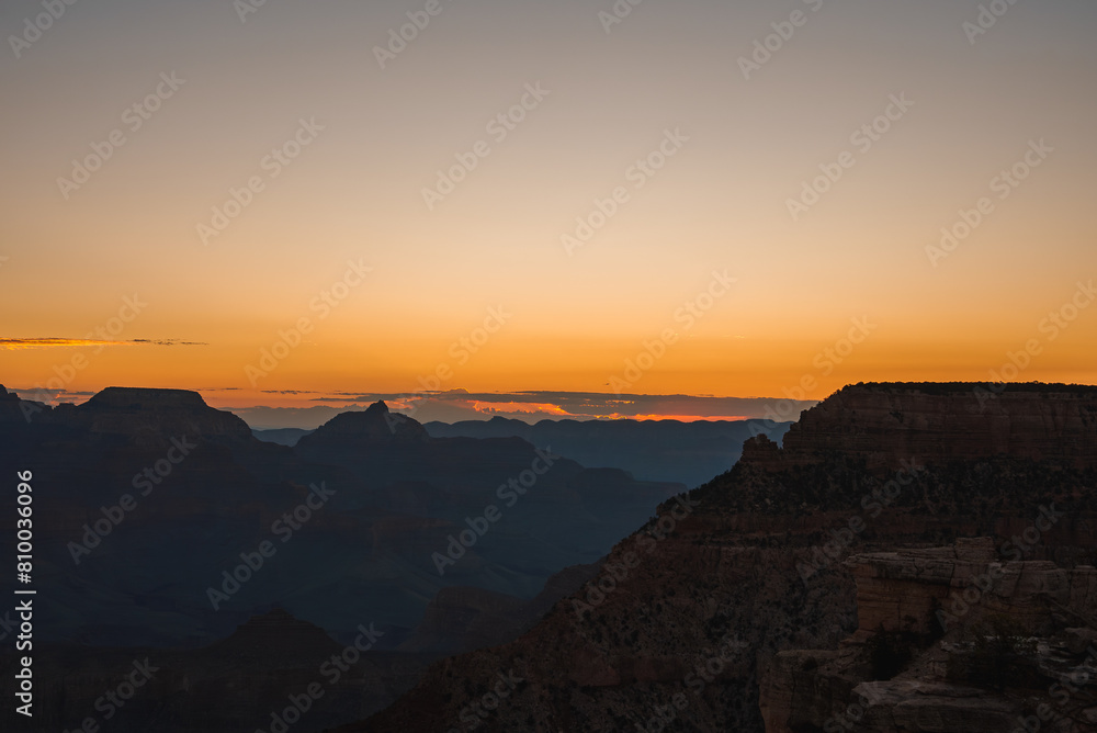 Scenic sunset over vast canyon with warm gradient colors from orange to blue. Silhouettes of rock formations visible against twilight sky. Possibly Grand Canyon viewpoint. Breathtaking natural beauty.