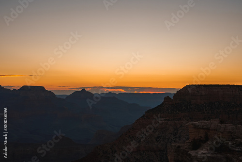 Scenic sunset over vast canyon with warm gradient colors from orange to blue. Silhouettes of rock formations visible against twilight sky. Possibly Grand Canyon viewpoint. Breathtaking natural beauty. © Aerial Film Studio