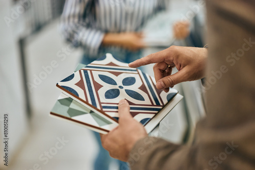 Close-up photo of a male seller holding some samples of ceramic tiles. (ID: 810051293)