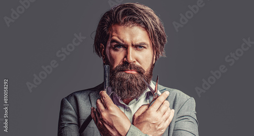 Handsome brutal man barber with beard and moustache hold barbershop retro razor blade and scissors  hair salon. Vintage barber shop  shaving. Man hairdresser holding a sharp professional scissors