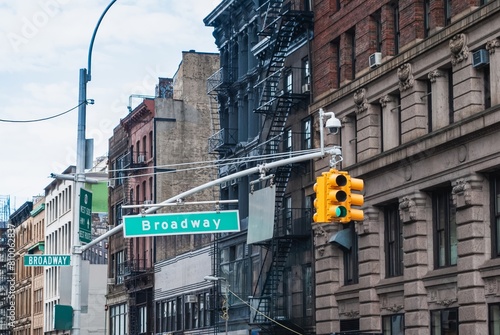 A street sign for Broadway is above a yellow traffic light
