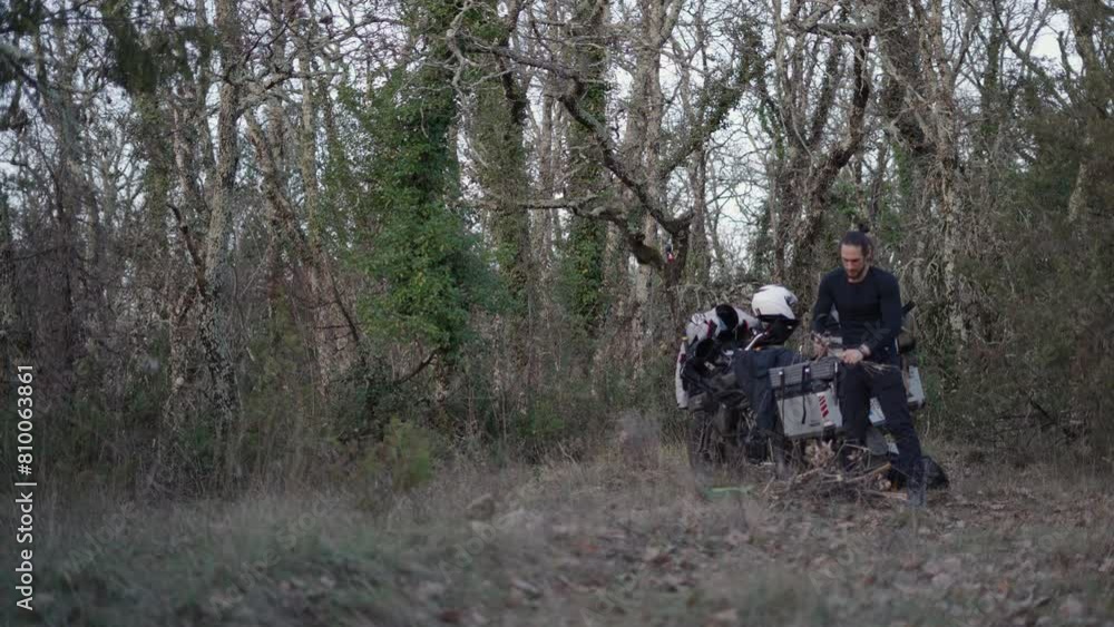 slow motion young caucasian man dressed in black breaking small dry branches with his hands to prepare a fire in the bush next to his motorcycle slow motion young caucasian man dressed in black breaking small dry branches with his hands to prepare a fire in the bush next to his motorcycle