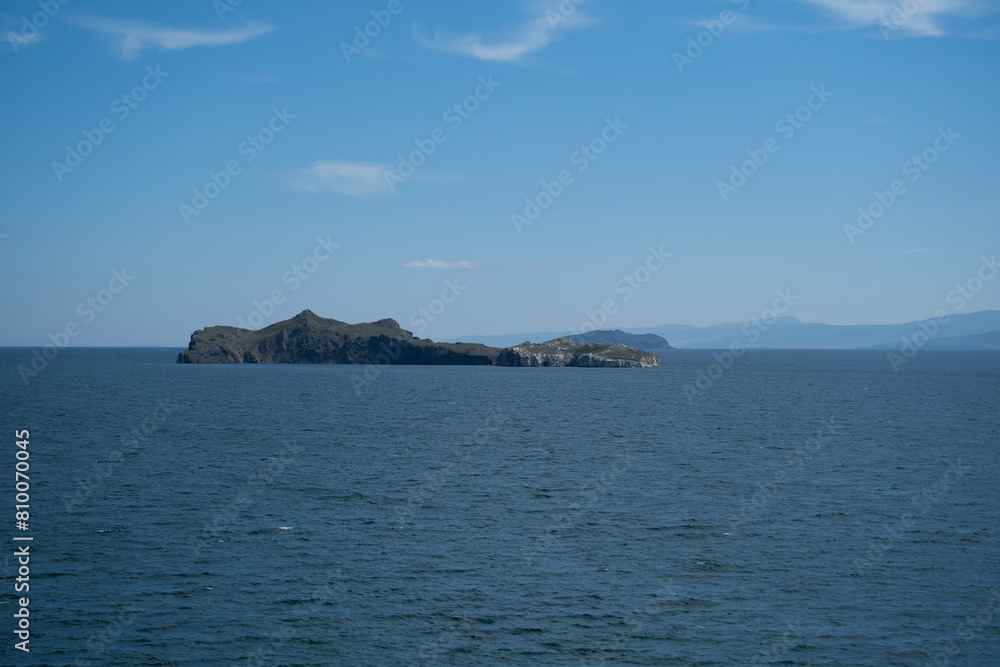 Water landscape,distant view of rocky uninhabited Lake Baikal island,on horizon faintly visible mountains of opposite shore, summer sunny day. Beautiful wild nature travel concept. Deep waves surface. Water landscape,distant view of rocky uninhabited Lake Baikal island,on horizon faintly visible mountains of opposite shore, summer sunny day. Beautiful wild nature travel concept. Deep waves surface.