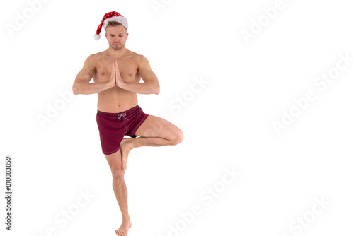 Christmas and New Year. A young attractive man with an athletic body is doing fitness wearing a Santa Claus hat. White background. photo