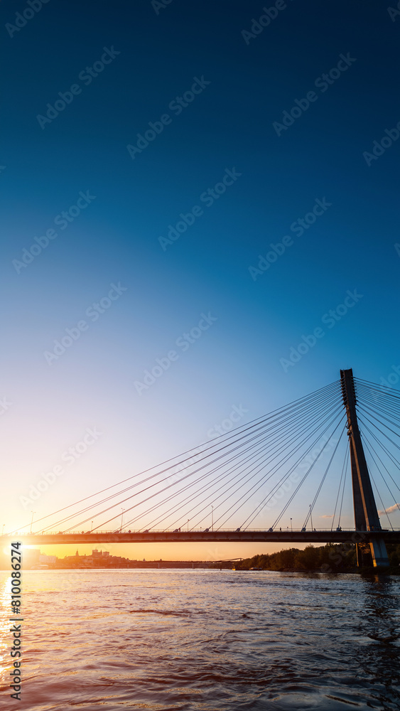 modern cable bridge over Vistula river at sunset, contemporary structures of Warsaw, blue sky on background