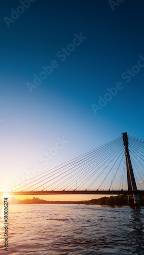 modern cable bridge over Vistula river at sunset, contemporary structures of Warsaw, blue sky on background © goami