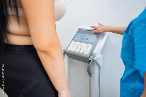 Overweight female patient being assisted by a nurse during a routine health check-up in a bright clinical setting