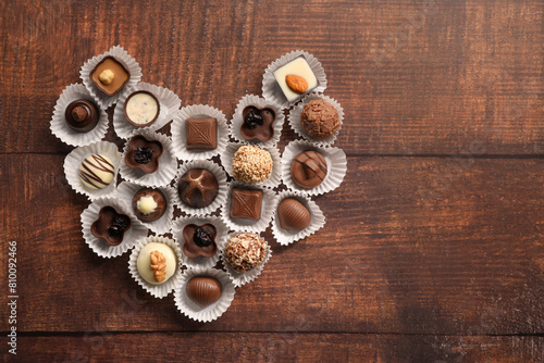 Heart made with delicious chocolate candies on wooden table  top view. Space for text