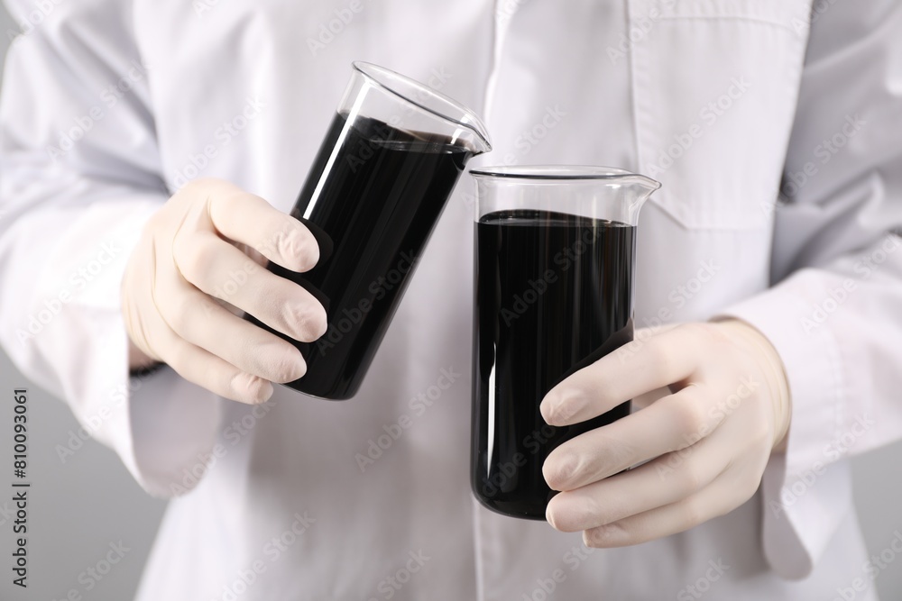 Woman pouring black crude oil into beaker on light background, closeup Woman pouring black crude oil into beaker on light background, closeup