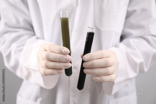Woman holding test tubes with different types of crude oil on light background, closeup photo